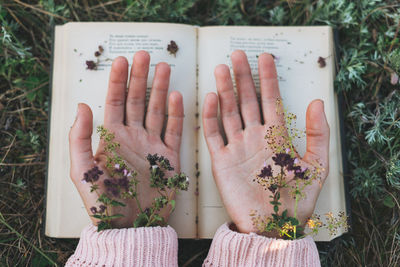 Directly above shot of woman hand with flower and book outdoors