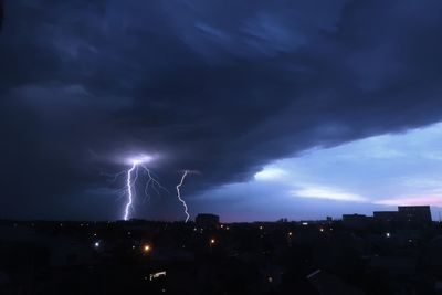 Low angle view of illuminated cityscape against dramatic sky