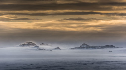 Scenic view of sea by snowcapped mountain against sky during sunset