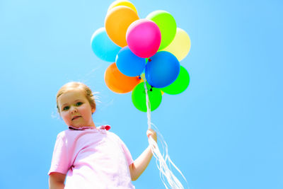 Low angle view of girl with balloons against blue sky