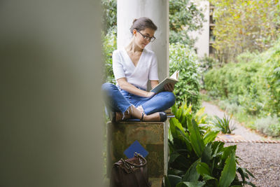 Young woman sitting on seat against plants