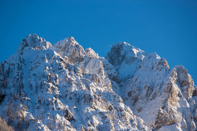 Low angle view of snowcapped mountains against clear blue sky