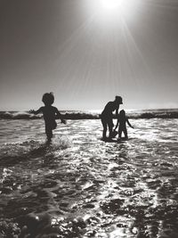 Silhouette mother with children enjoying in sea on sunny day