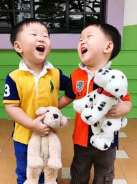 Cute twins smiling with stuffed toys on against house