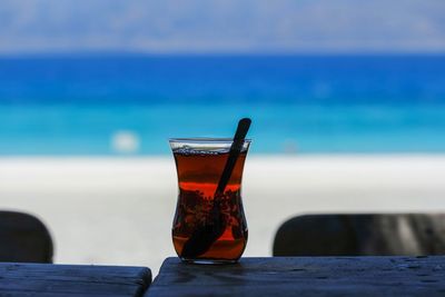 Close-up of drink on table at beach against blue sky