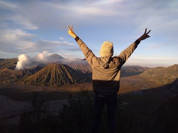 Rear view of man with arms raised against sky