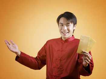 Portrait of man holding cards while standing against orange background