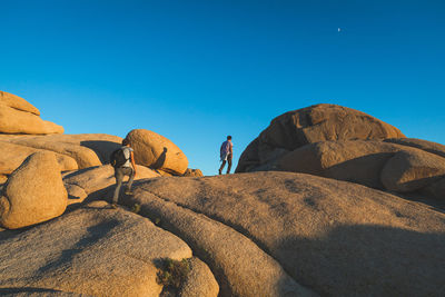 Rear view of men on rock against clear blue sky