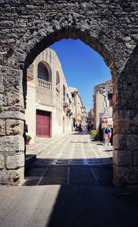 Diminishing perspective of alley amidst old buildings against blue sky during sunny day