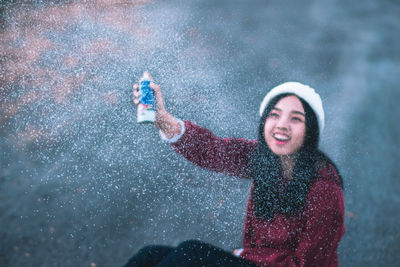 High angle close-up of smiling young woman spraying in snow