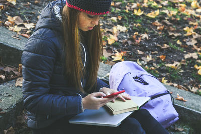 Girl with wool cap sitting in the park use smartphone student teen doing homework with phone outdoor