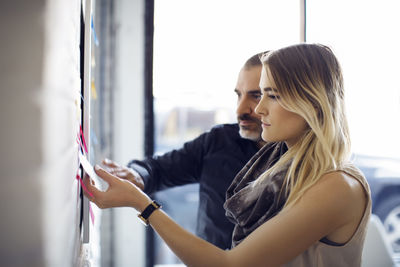 Business people sticking adhesive notes on wall at creative office