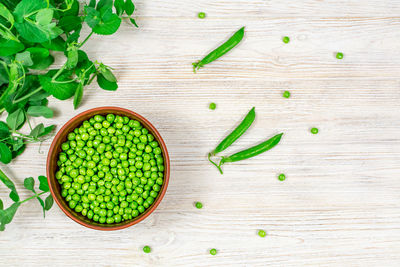 Fresh green peas in a bowl against the background of leaf shoots, sprigs of young green peas. 