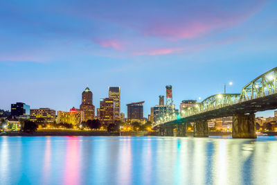 Illuminated buildings by river against sky at night