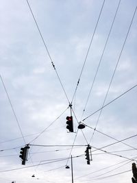 Low angle view of stoplights hanging against cloudy sky