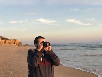 Side view of woman photographing against sky during sunset