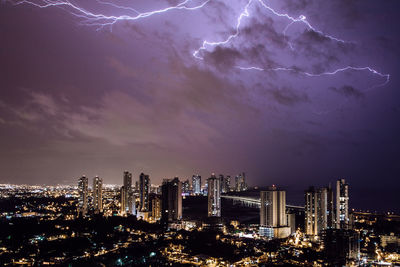Illuminated cityscape against sky at night with thunder storm