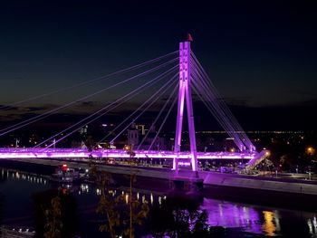 Illuminated bridge over river against sky at night