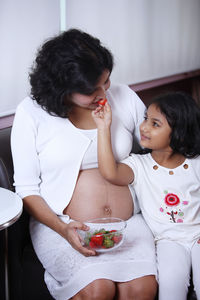 Cute girl feeding strawberry to pregnant mother at home