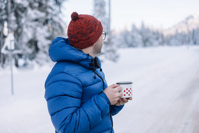 Man drinking hot tea while being on a road trip in the mountains in winter time.