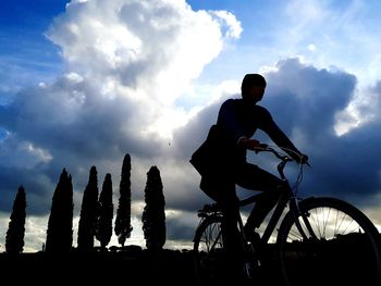 Low angle view of silhouette man riding bicycle against sky