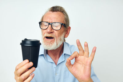 Smiling senior man holding disposable coffee cup against white background