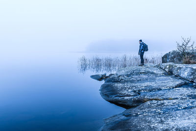 A lone hiker admires the beauty of nature reflected in a tranquil lake, surrounded by misty skies 