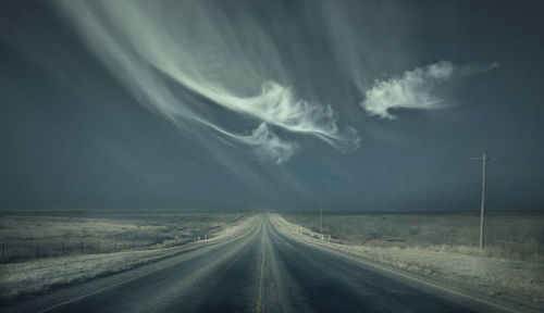 Country road on field against cloud pattern in sky