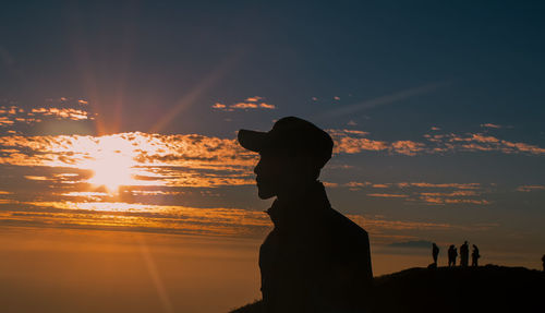 Silhouette of a bearded man with hat up in the hill in the sunset