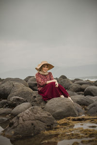 Woman on rock at beach against sky