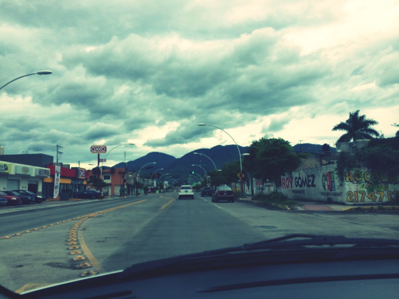 transportation, car, sky, road, land vehicle, cloud - sky, mode of transport, street, cloudy, road marking, the way forward, cloud, building exterior, tree, street light, architecture, built structure, on the move, travel, diminishing perspective