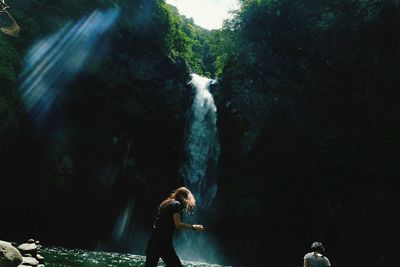 Rear view of woman standing on rock against waterfall