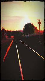 Empty road along trees and orange sky