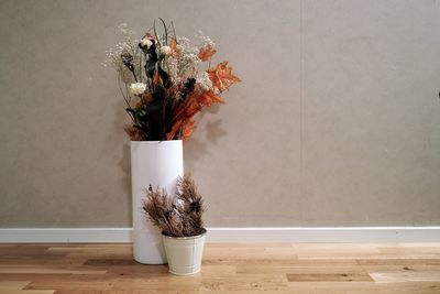 Artificial flowers in vase on floor against wall