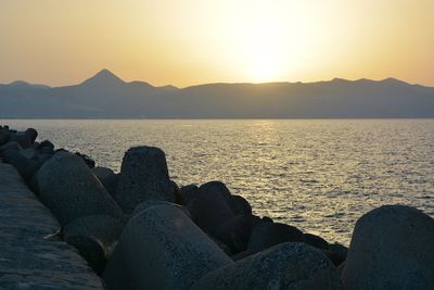 Low section of rocks on sea against sunset sky