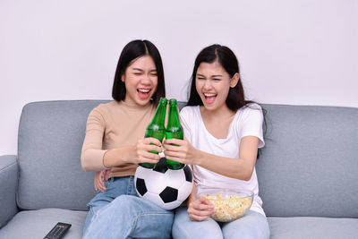 Happy friends watching sports while sitting on sofa against wall