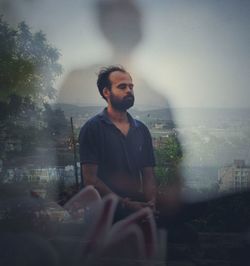 Young man looking away while sitting in rain against sky