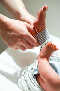 Cropped hands of person removing clothes of baby lying on bed