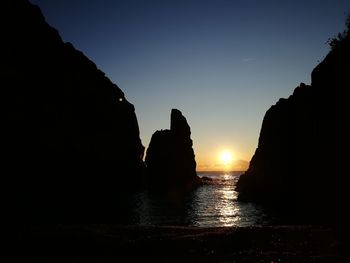 Silhouette rocks by sea against clear sky during sunset