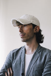 Thoughtful male architect wearing cap and blazer against white wall