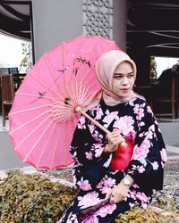 Woman holding pink umbrella while sitting outdoors