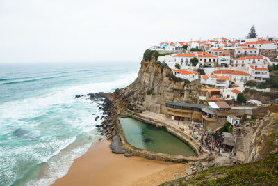 Buildings in town by sea against sky