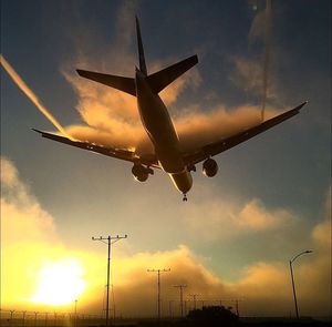 Low angle view of silhouette airplane flying against sky during sunset