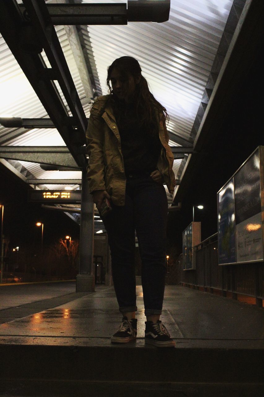 WOMAN STANDING ON ILLUMINATED UNDERGROUND WALKWAY