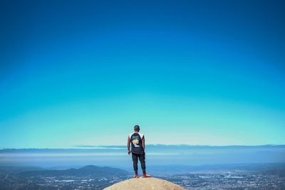 Rear view of man standing against blue sky