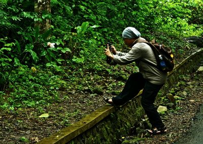 Side view of man photographing flower while standing by roadside