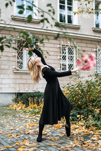 Ballerina dancing in autumn city street, modern ballet dancer in black dress, pointe shoes outdoors