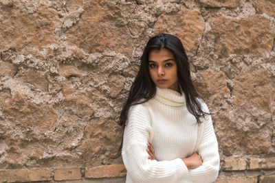 Portrait of a young woman standing against wall