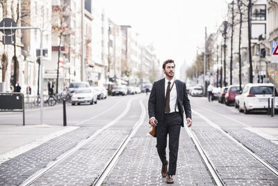 Full length of businessman walking by railroad tracks in city