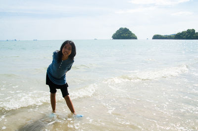 Full length portrait of smiling young woman standing at beach